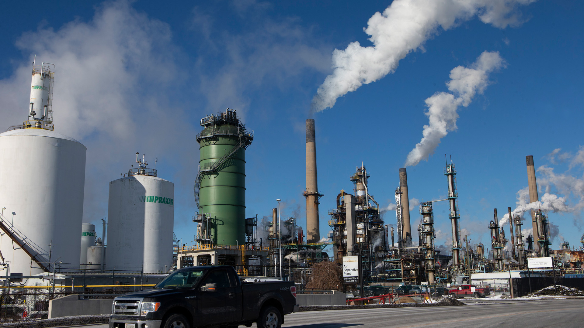 White plumes of steam are released into the sky at the Imperial Oil plant, made up of a cluster of wide, round towers and skinny tanks.