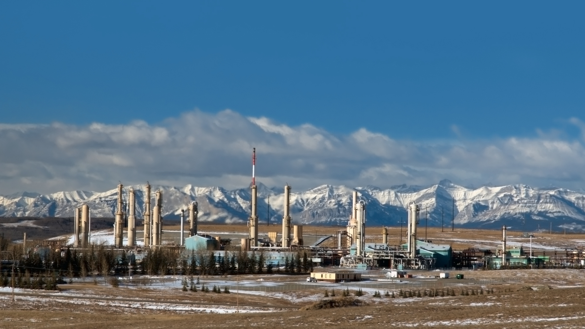 A gas plant near Cochrane Alberta is pictured in front of a snow-capped mountain range.