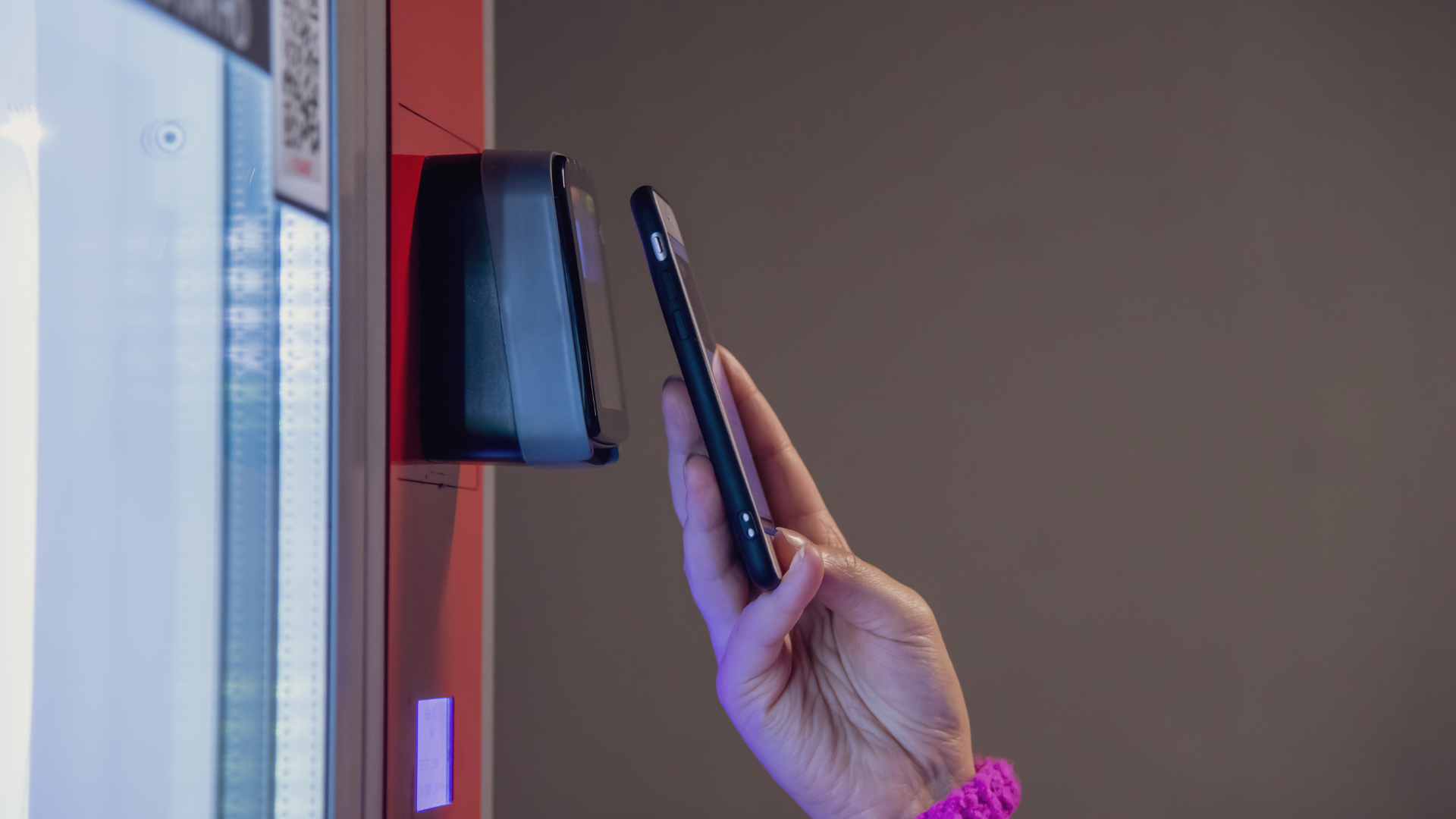 Close up view of woman paying for purchase at snack vending machine using smartphone.