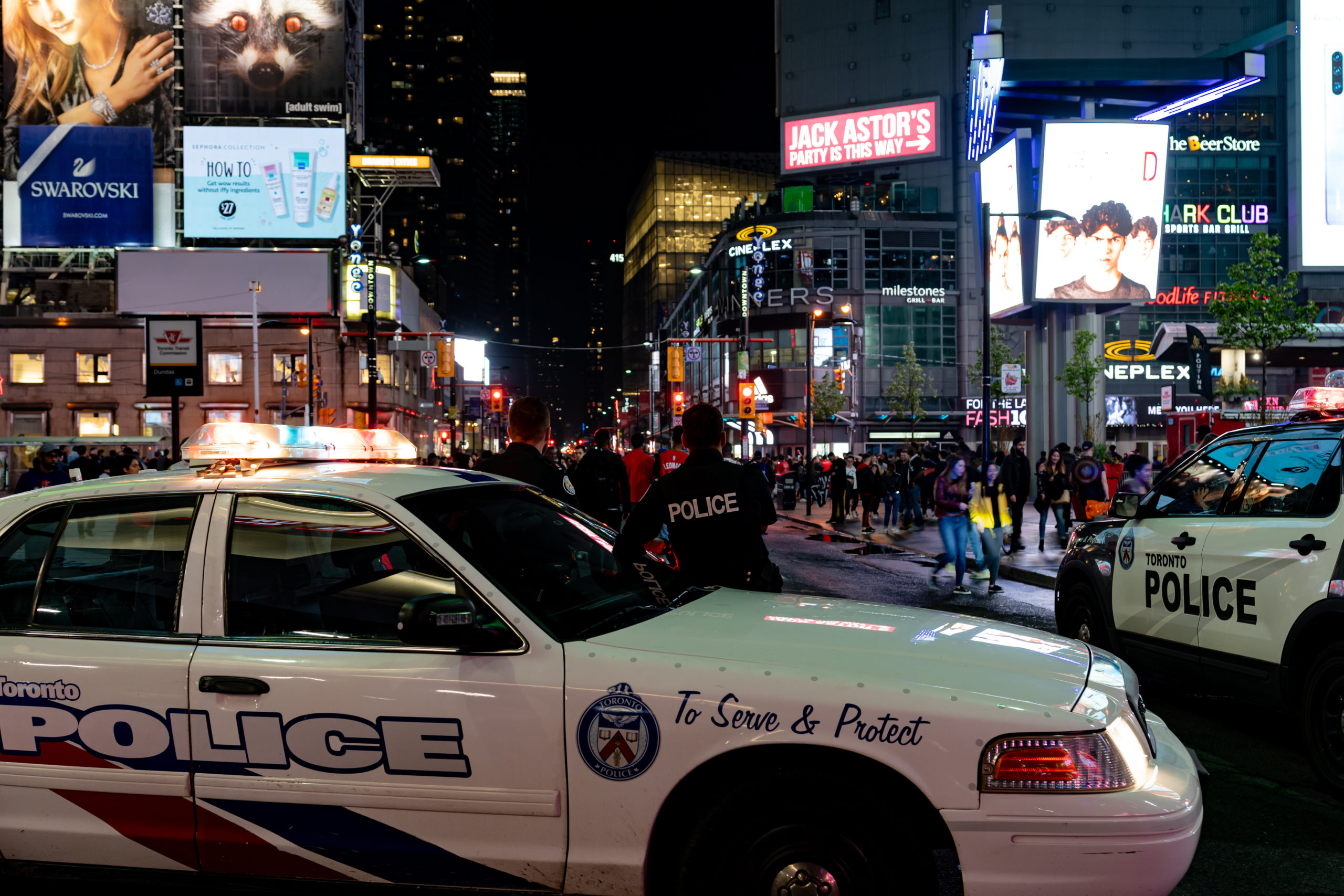 Two police vehicles are parked as an officer watches evening crowds in downtown Toronto.