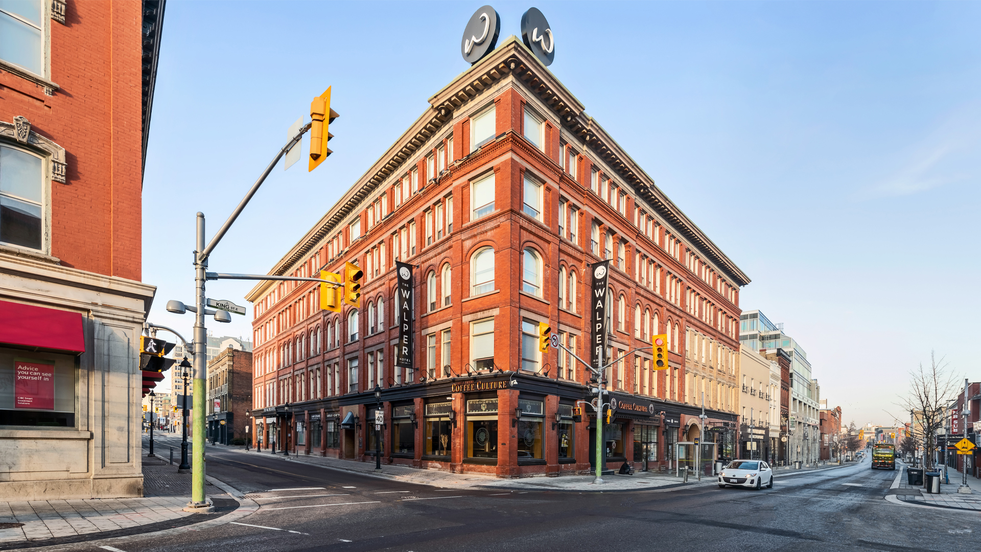 On a downtown street corner, an elegant five-storey building sits, made from red brick with windows that have curved tops.