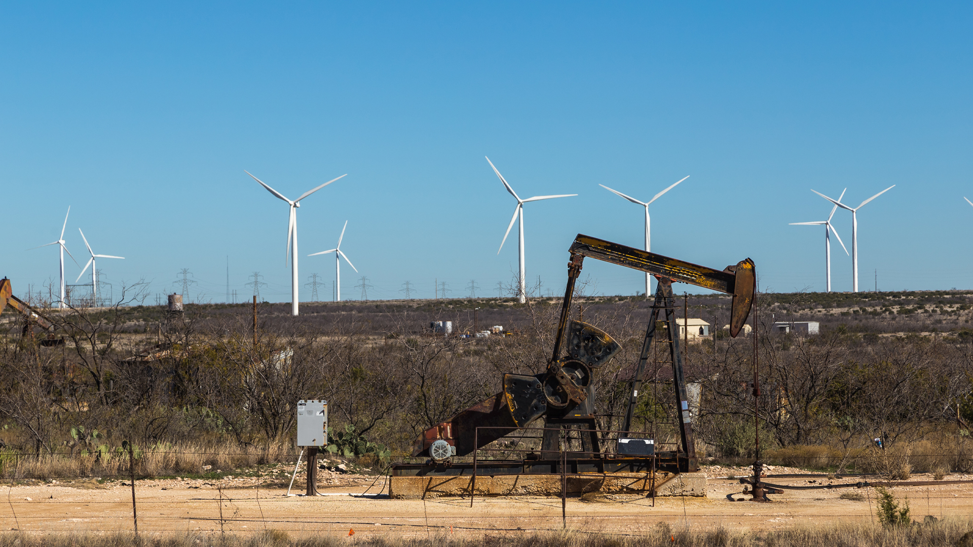 An oil pump in the foreground with wind turbines in the background.