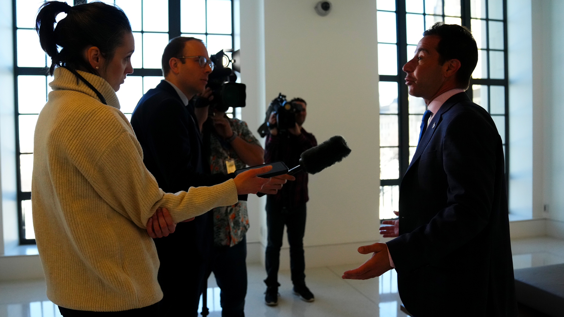 Deux journalistes tiennent des micros près du visage d’Anthony Housefather, et deux hommes munis de caméras vidéo filment l’entretien, qui se déroule dans une salle lumineuse avec de grandes fenêtres et des sols en marbre.