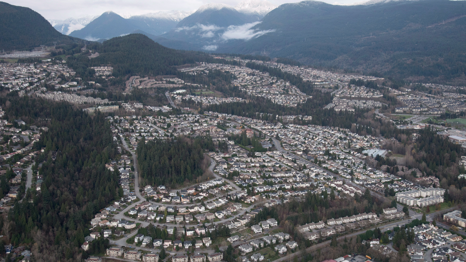 From the air, a sprawling subdivision covers several kilometres of land surrounded by swaths of forest and snow-capped mountains in the distance.