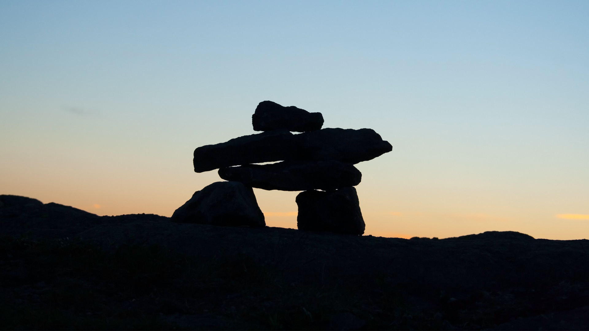 An Inukshuk is silhouetted against the last light of sunset.
