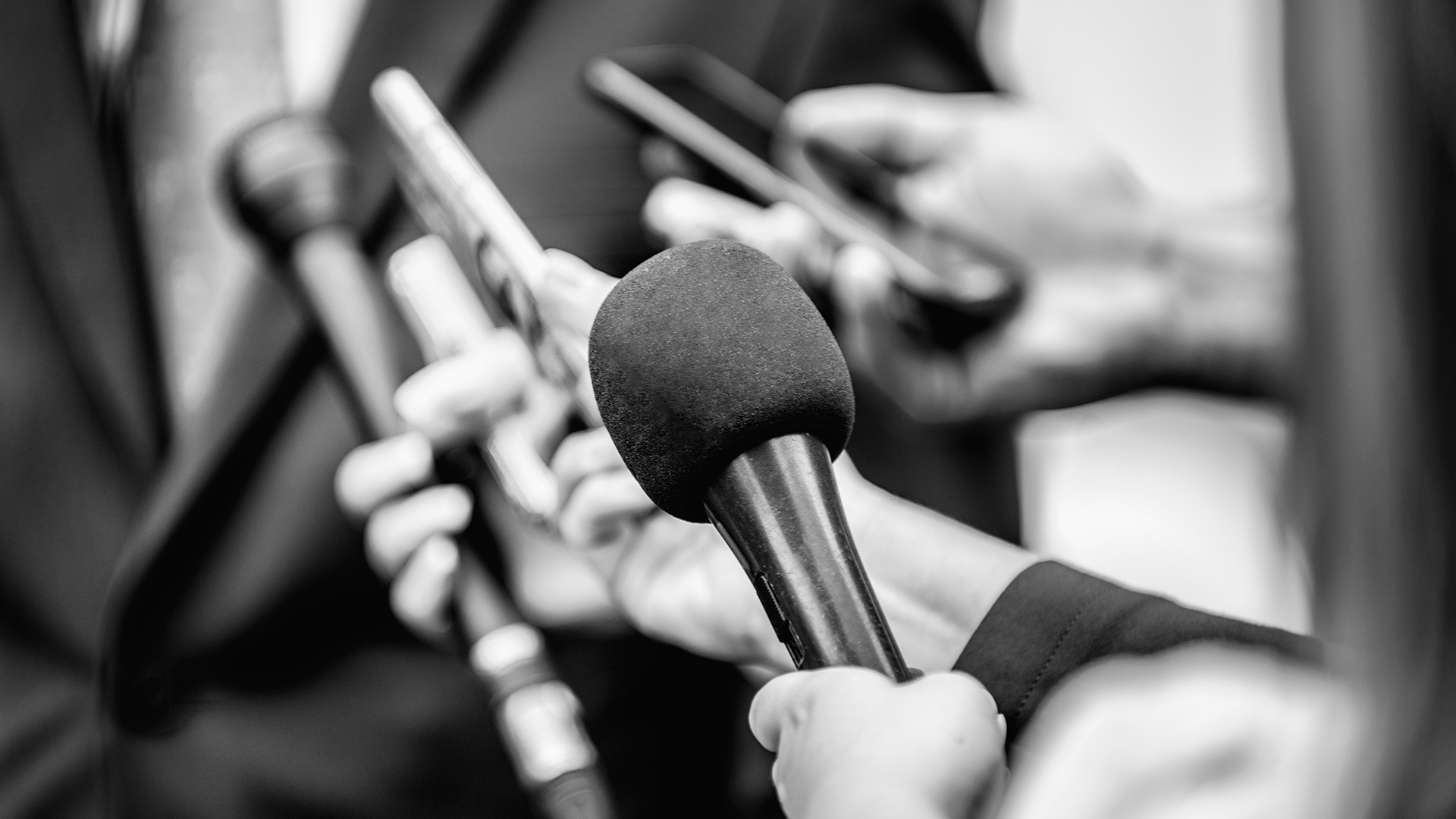 Media interview - journalists with microphones interviewing a formally dressed politician or businessman.