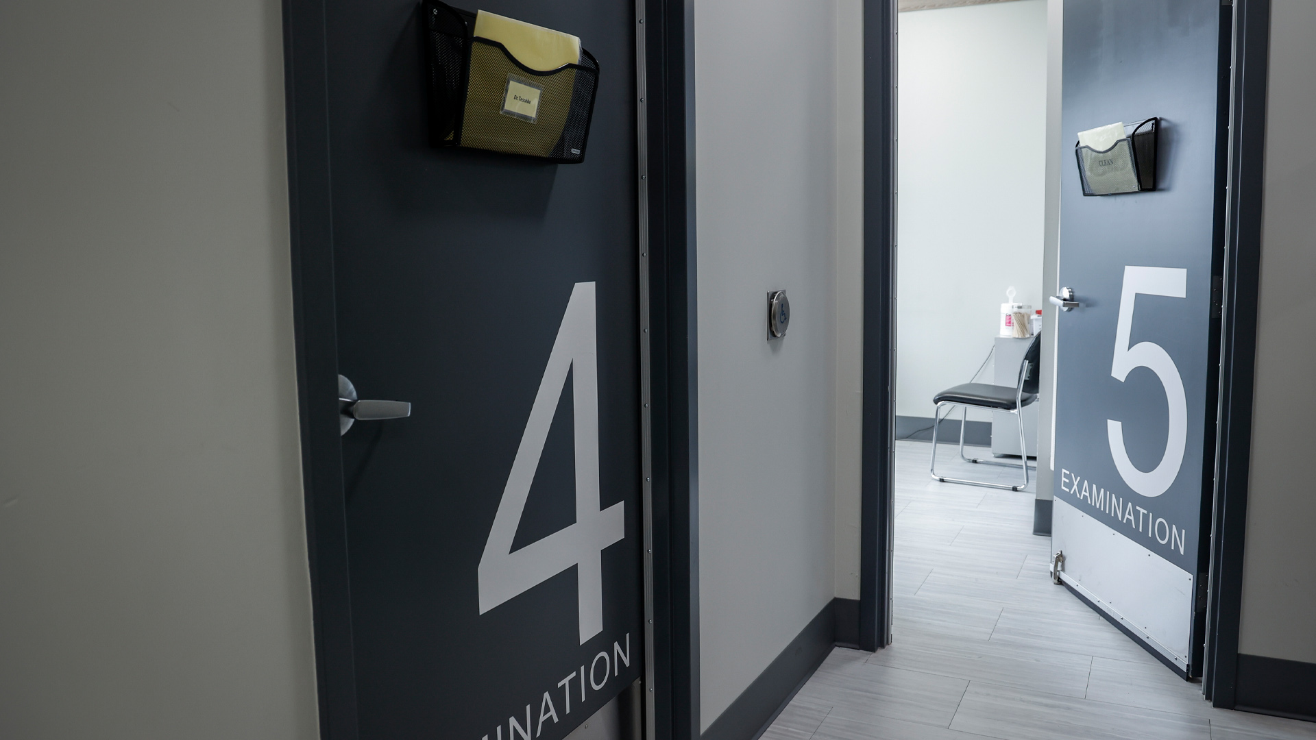 Au bout d'un court couloir se trouvent deux salles, chacune dotée d'une porte métallique gris foncé portant la mention " examen ". L'une est marquée d'un gros "4", l'autre d'un gros "5". Dans les deux cas, de petits paniers métalliques sont fixés pour contenir des dossiers.