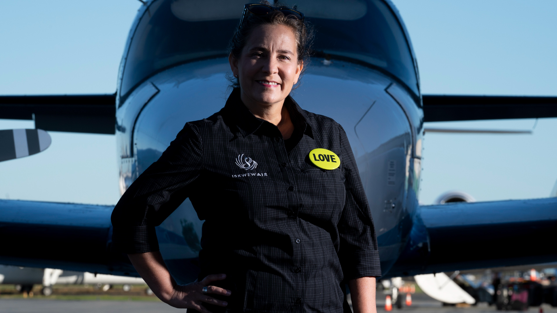 The pilot in a navy jumpsuit stands in front of a small twin-engine aircraft.