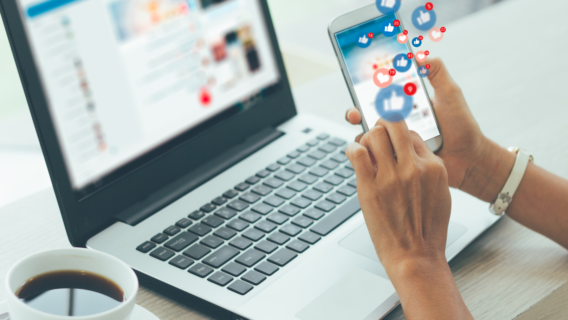 A woman using a smart phone to surf social networks. A computer is open and a cup of coffee is next to it.