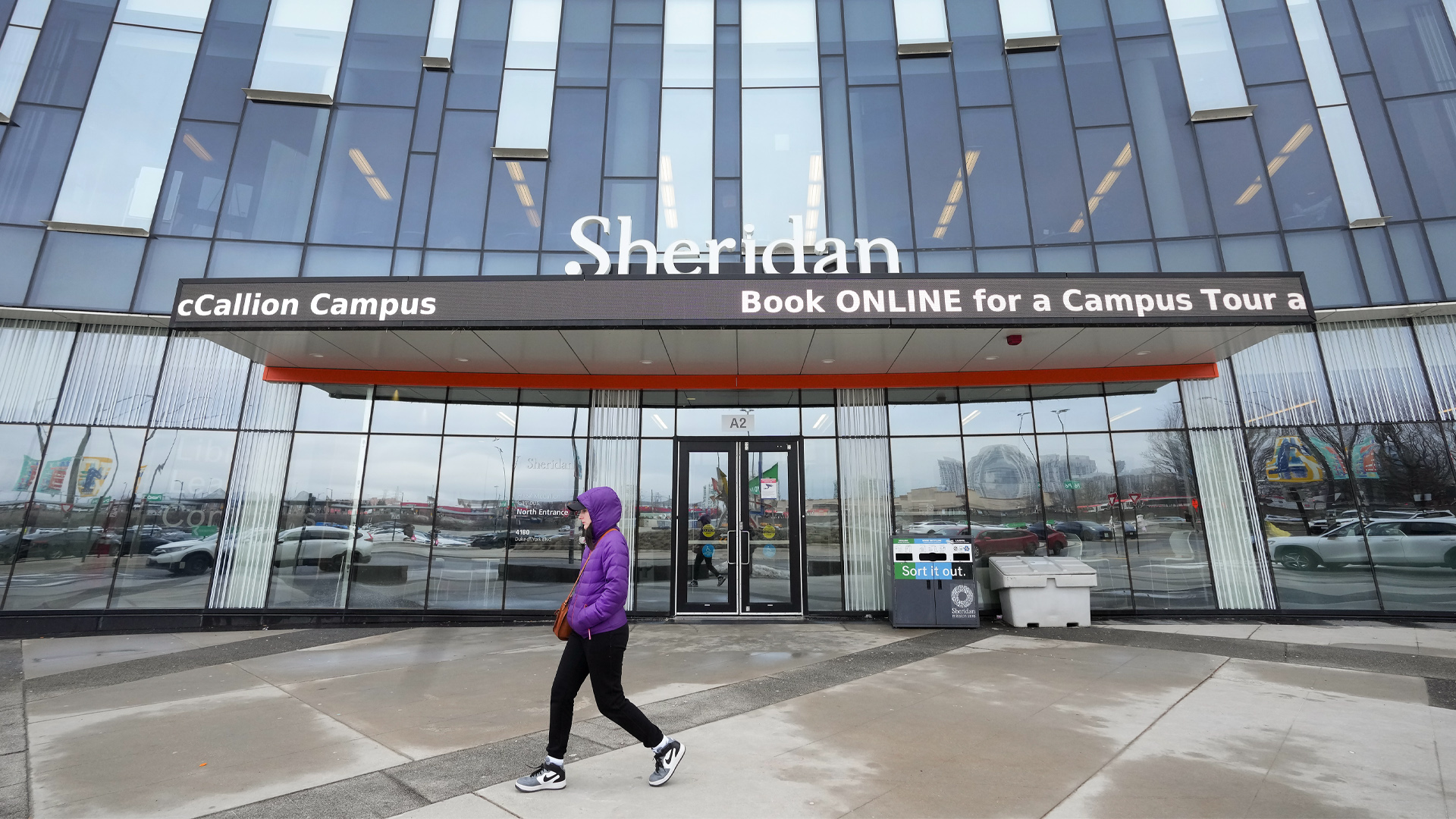Des étudiants portant des sacs à dos marchent devant le bâtiment bas en briques rouges surmonté d'un panneau indiquant "syndicat des étudiants".