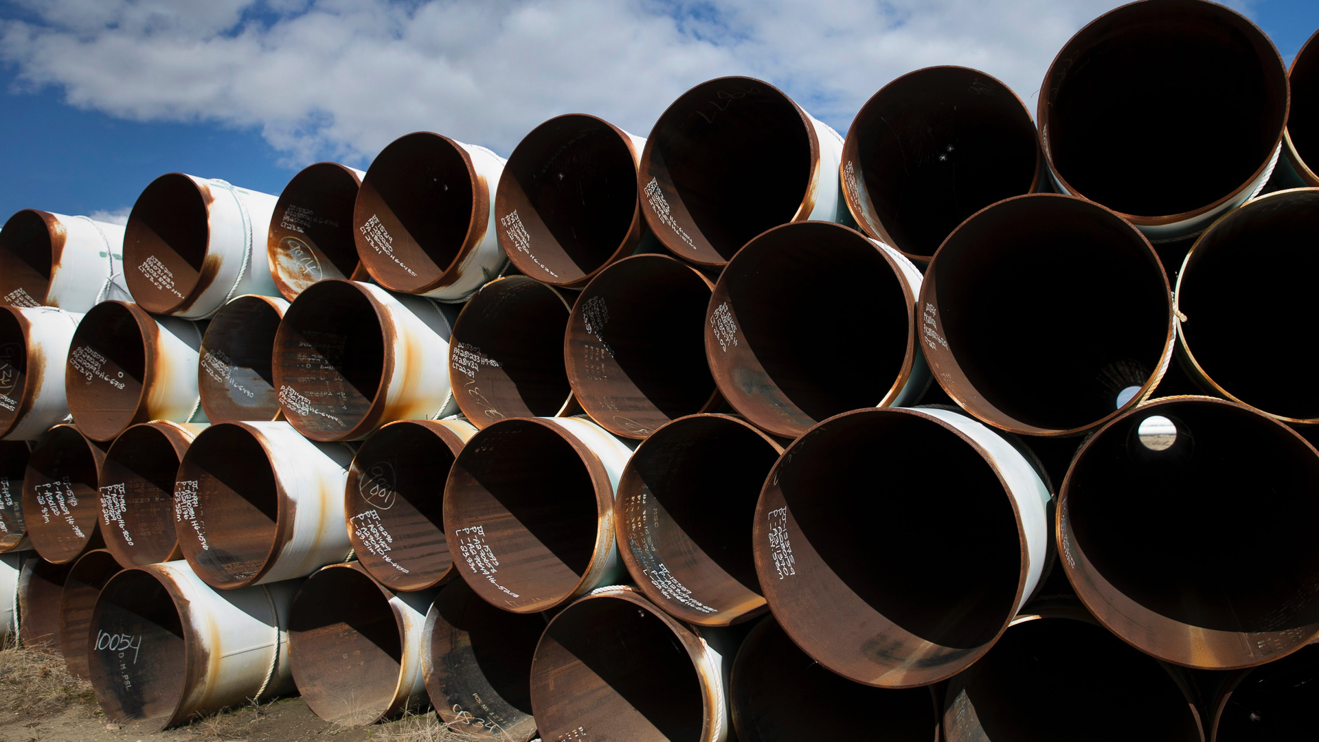 The rusted openings of dozens of rusting pipes stacked with a blue sky above.