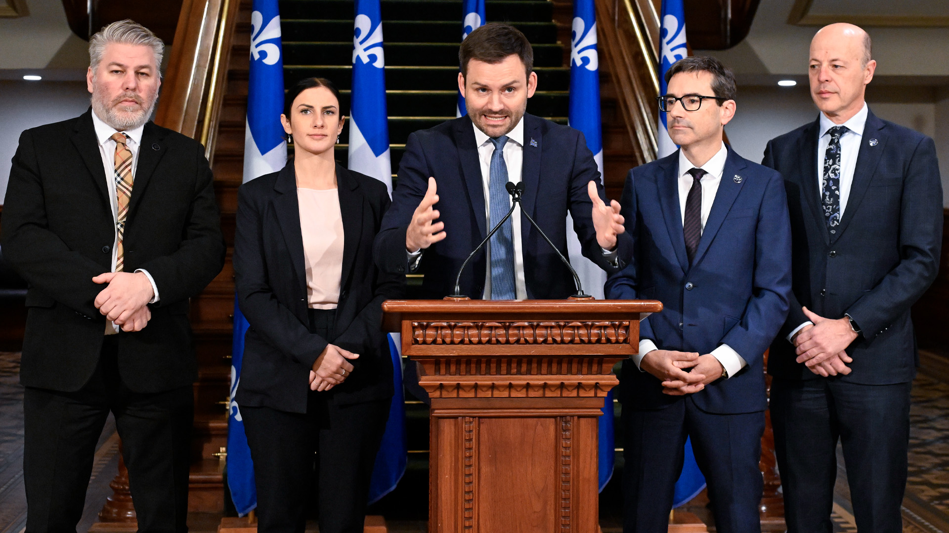 Le chef du PQ agite les mains en parlant alors qu'il est entouré de quatre membres de son parti.