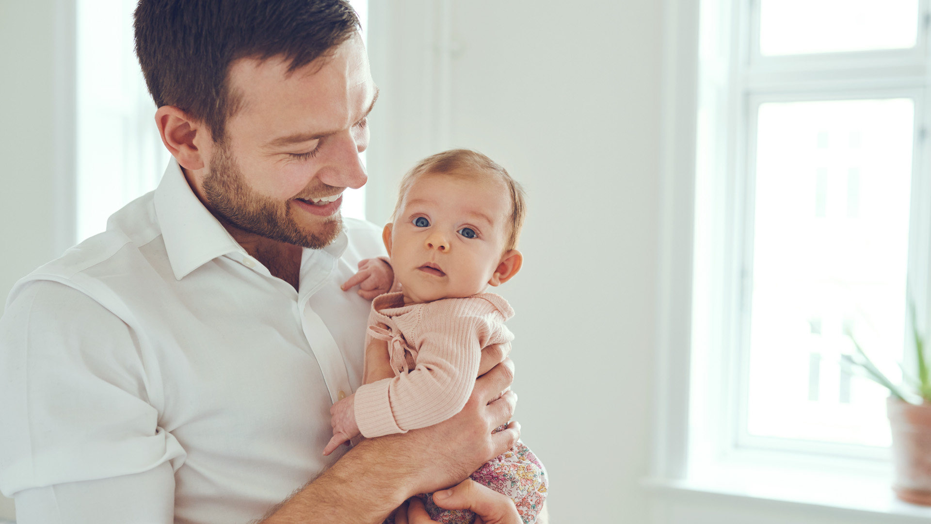 Un homme tient un poupon dans ses bras et le regarde en souriant. L’enfant regarde la caméra.