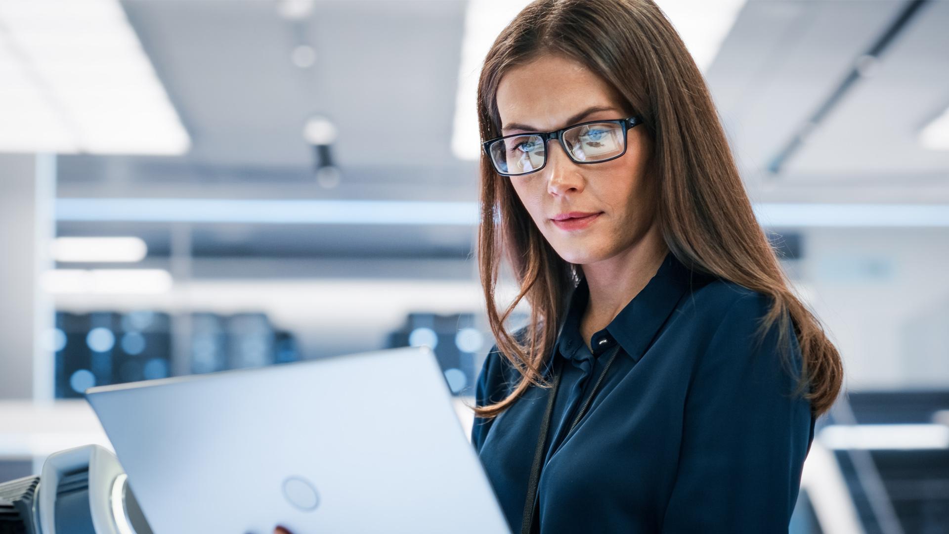Une jeune femme portant des lunettes se trouve dans un laboratoire. Elle regarde des données sur un ordinateur portable.