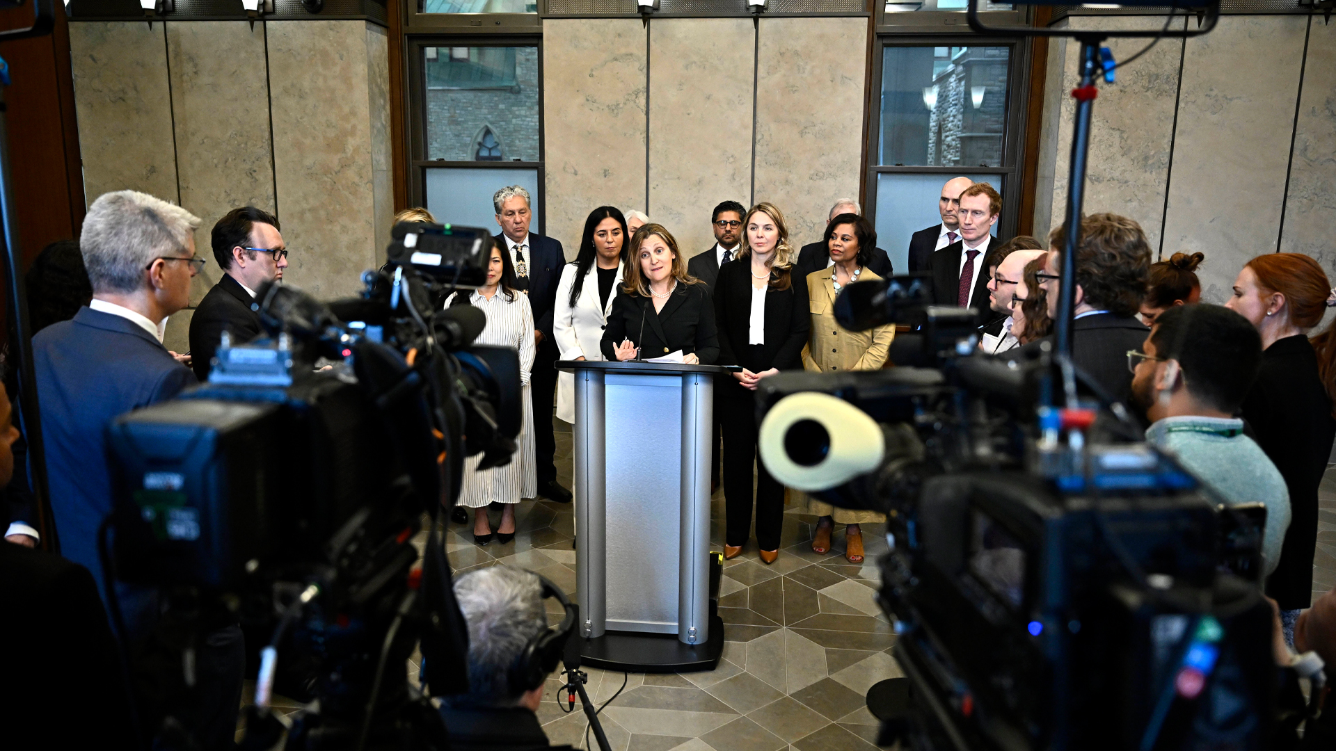 Freeland is at the podium with about a dozen people around her.