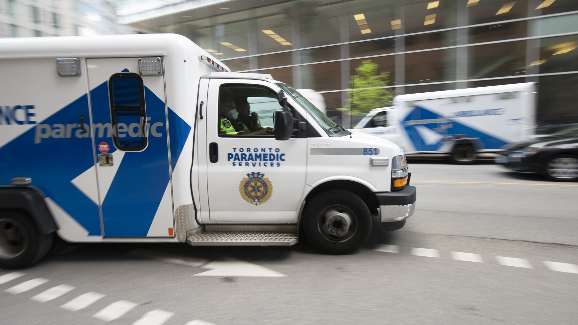 Le véhicule est blanc avec un marquage bleu. Le photographe a suivi l’ambulance en mouvement alors qu’elle passait devant un bâtiment vitré situé de l’autre côté de la rue, et qui est flou sur l’image.