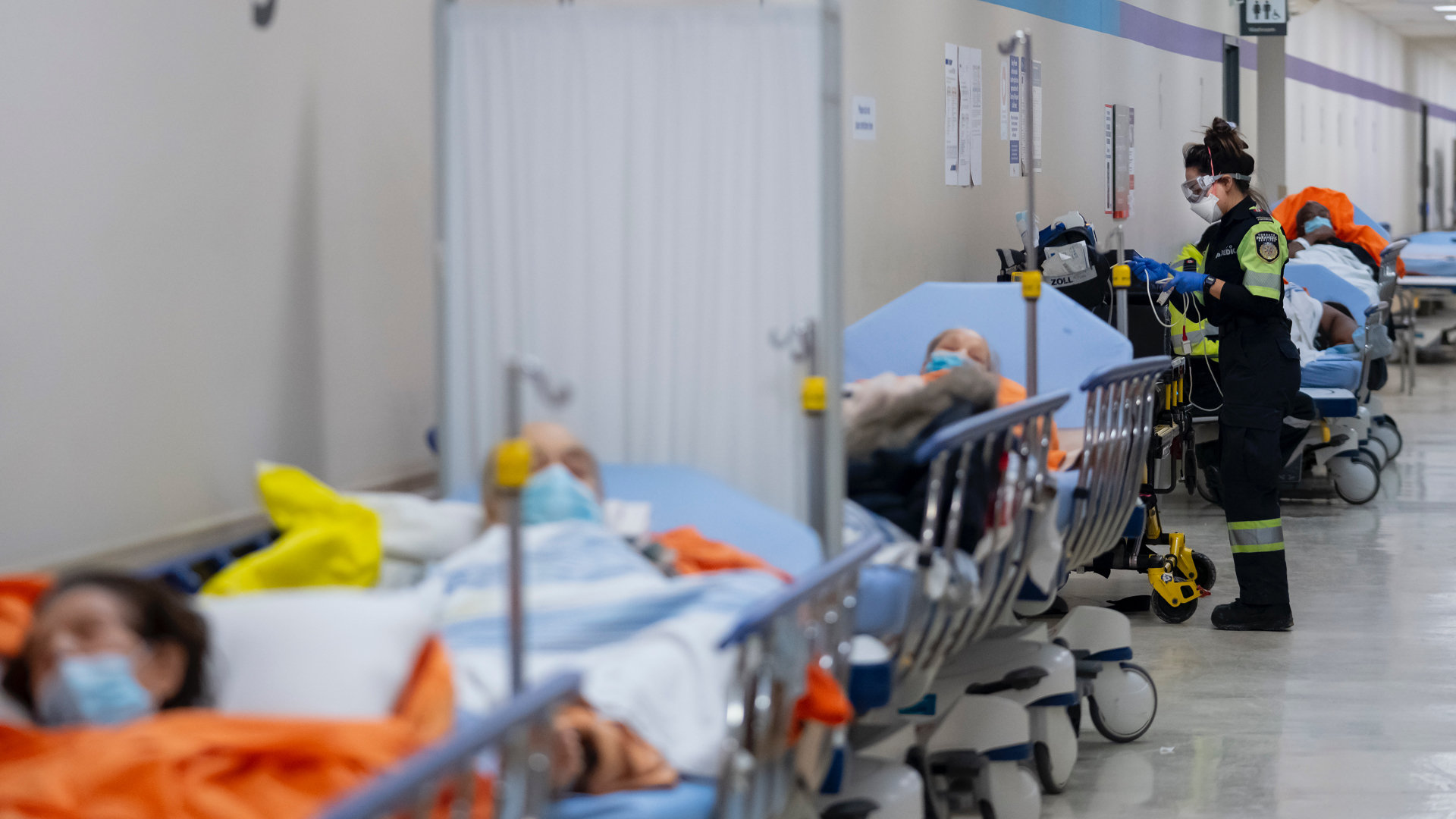 A paramedic stands among eight or nine patients in a hallway.