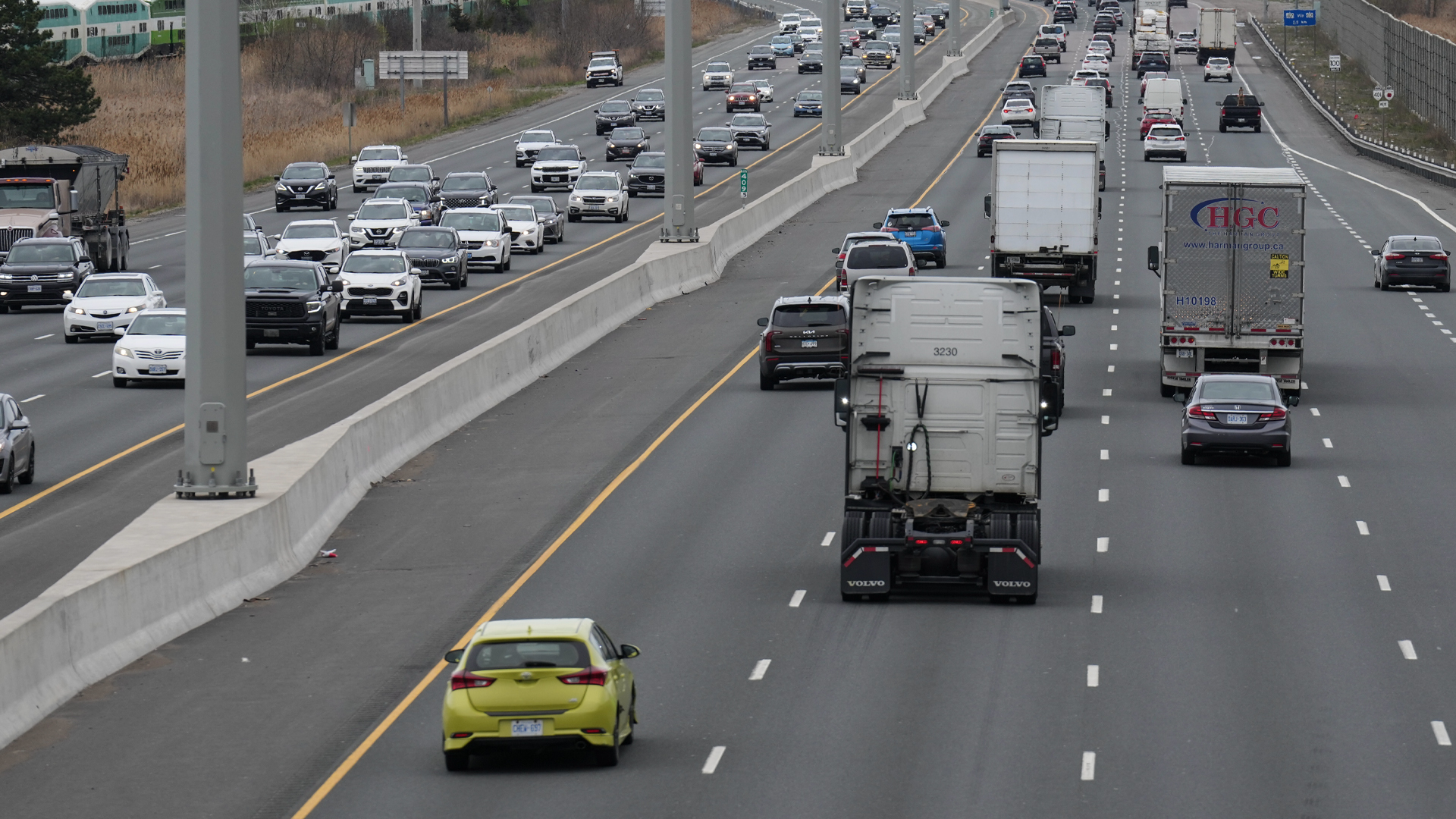 Eight lanes of traffic are shown. Most lanes are bumper to bumper. The green-and-white commuter train passes on tracks running parallel to the highway.