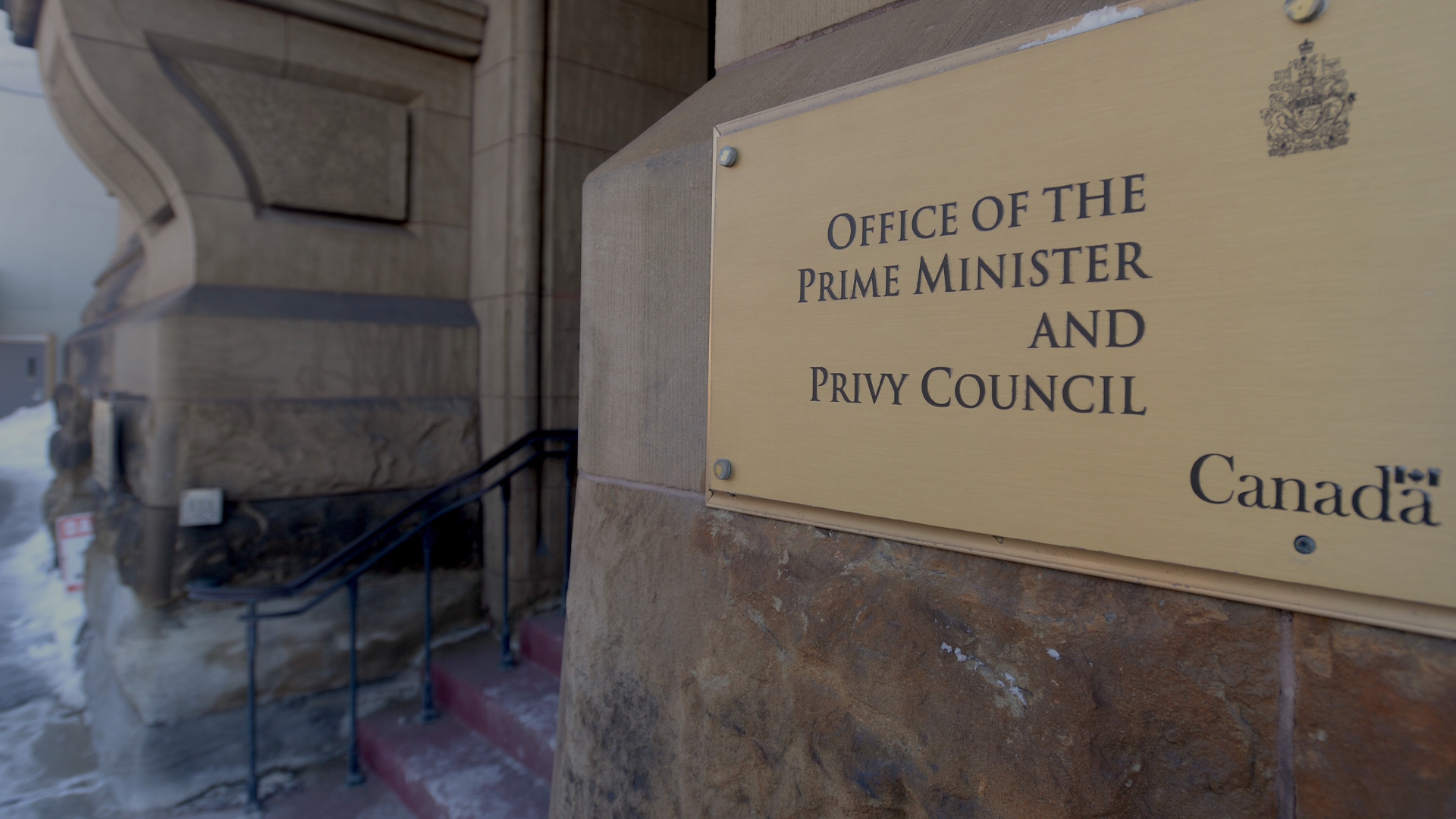 On an exterior carved stone wall, a plaque bearing the Canadian coat of arms indicates the entrance to the Prime Minister's office and the Privy Council.