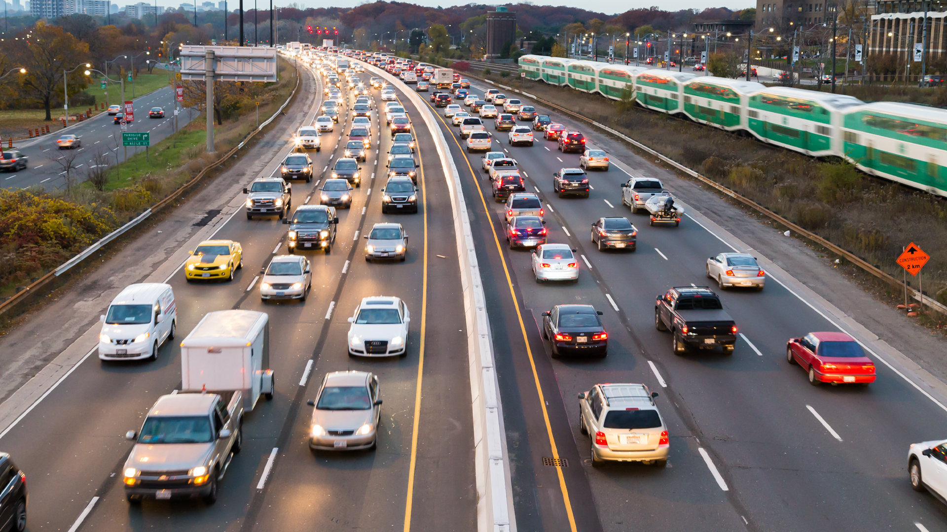 A photo of traffic on a three-lane highway with a train running alongside.