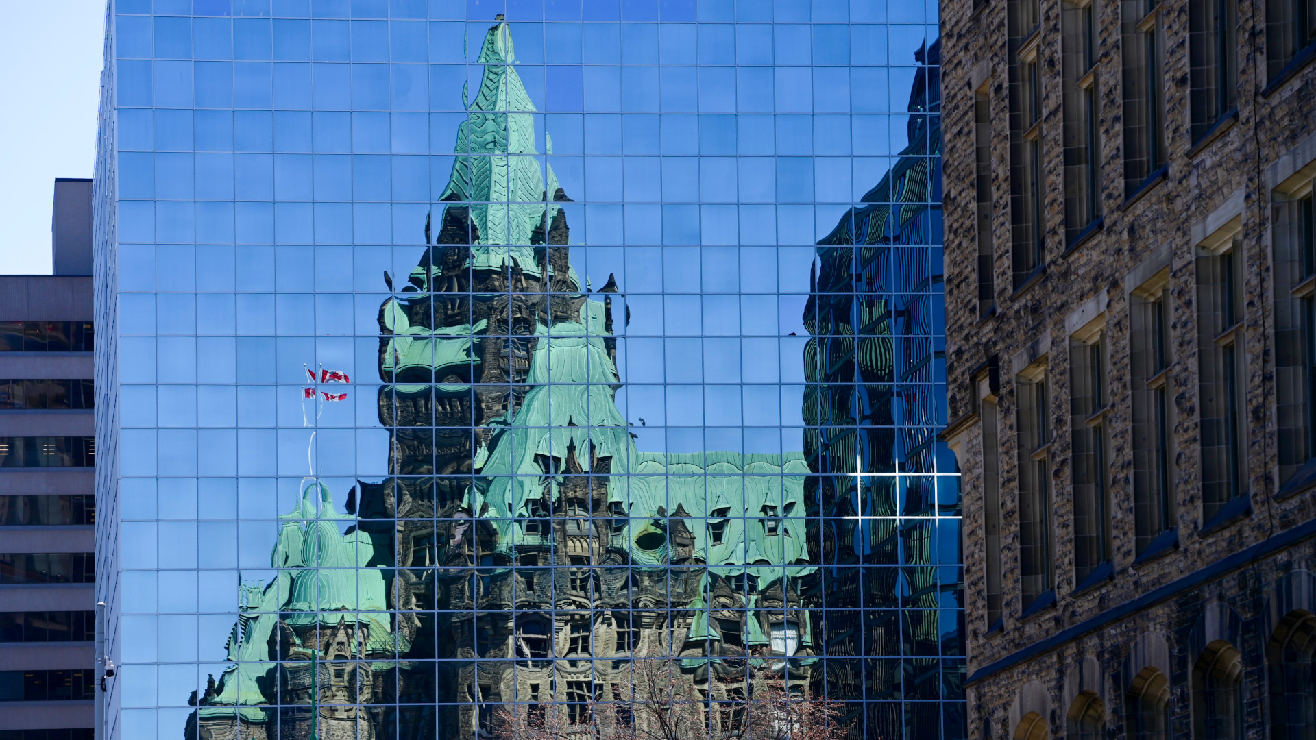 The heritage Confederation building is blurred in the reflection of a modern glass tower. 