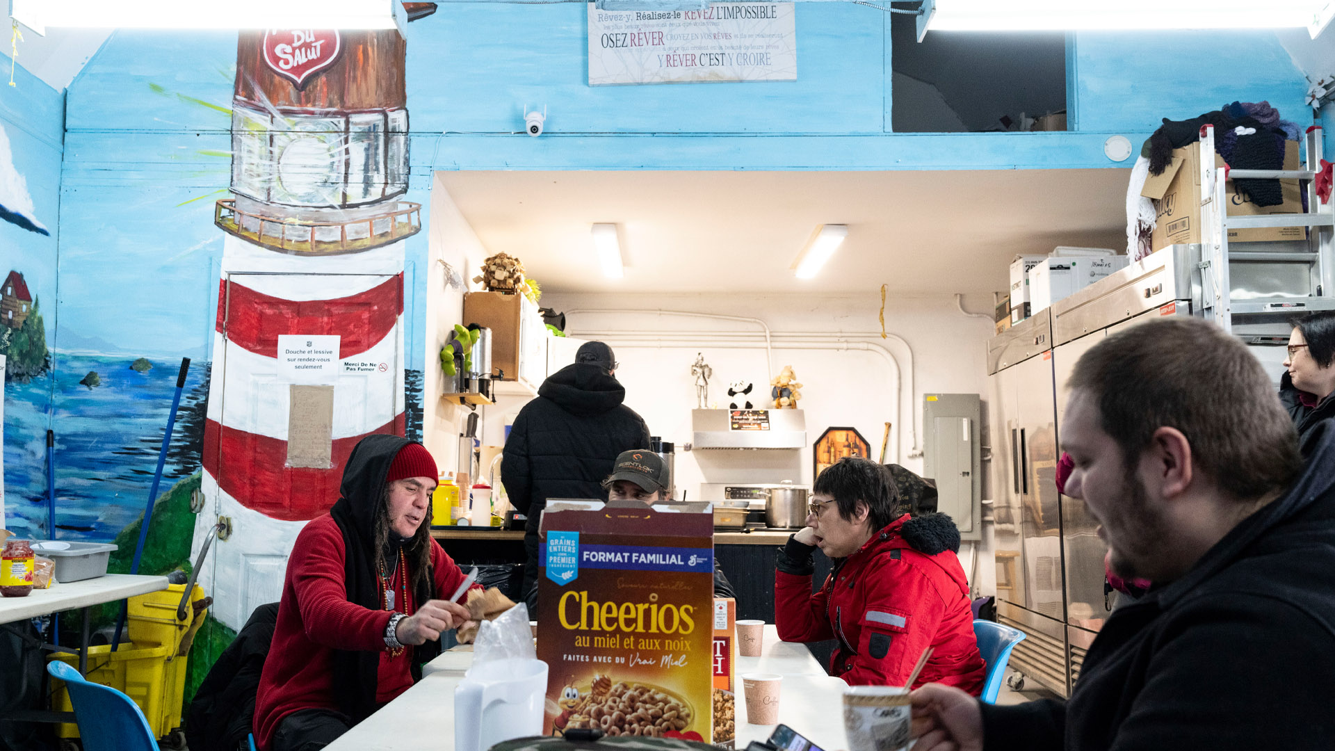 Quatre personnes mangent autour d'une table au milieu de laquelle se trouve une boîte de Cheerios.Une fresque murale représente un phare.