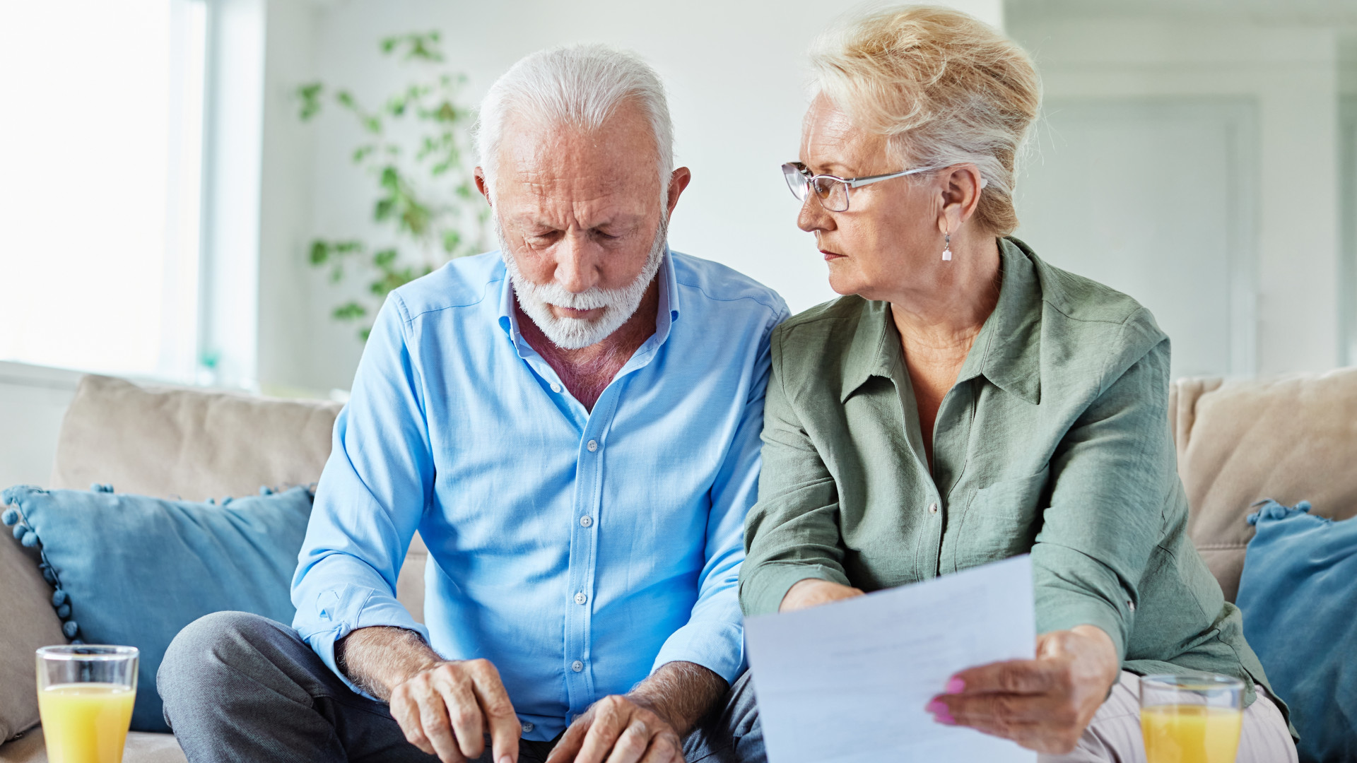 Un homme et une femme blancs d’un certain âge sont assis sur un canapé et consultent des feuilles de papier posées sur une table basse devant eux. Ils utilisent une calculatrice