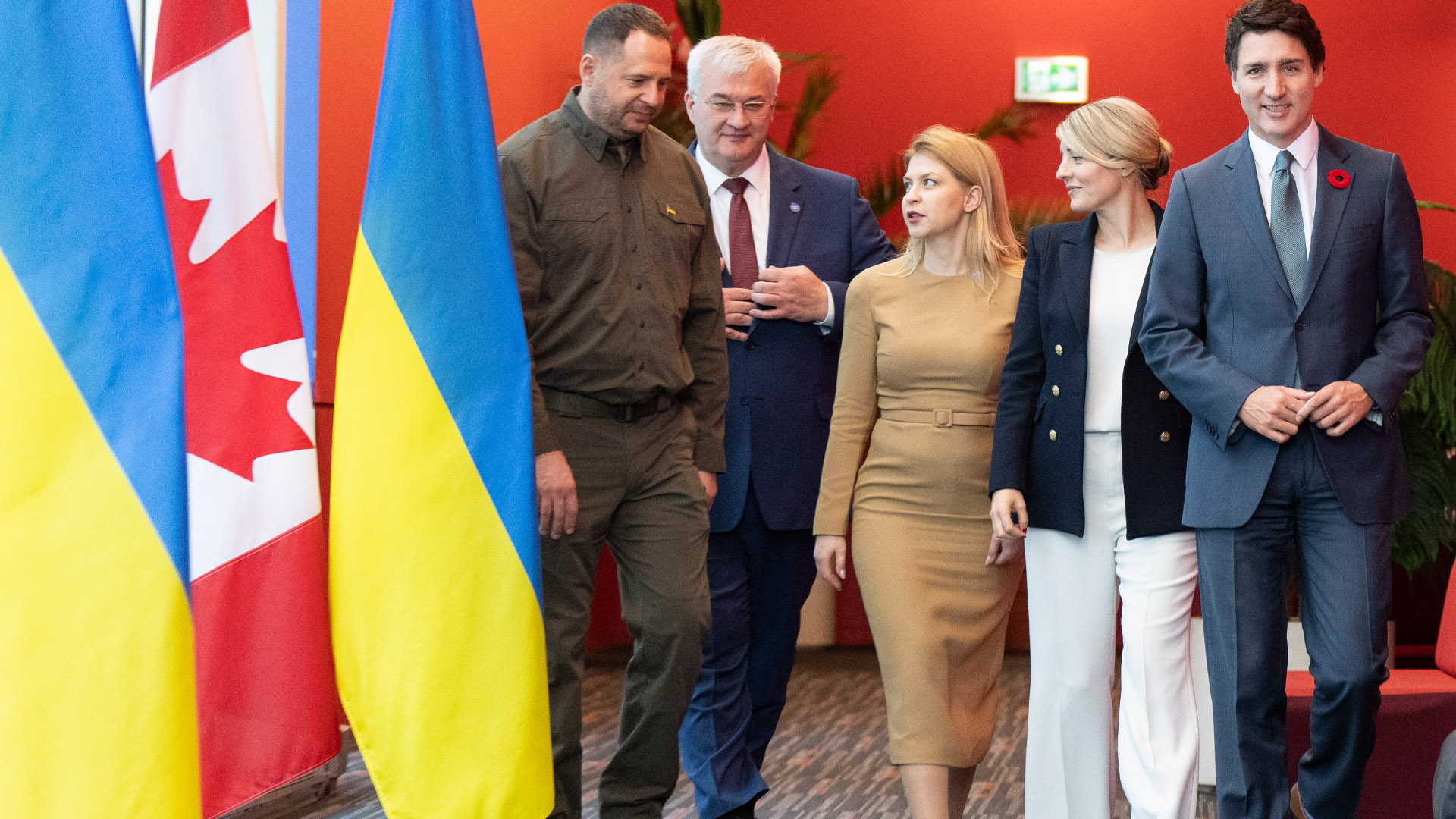 Ukrainian and Canadian flags are in the foreground as the ministers walk in line chatting.