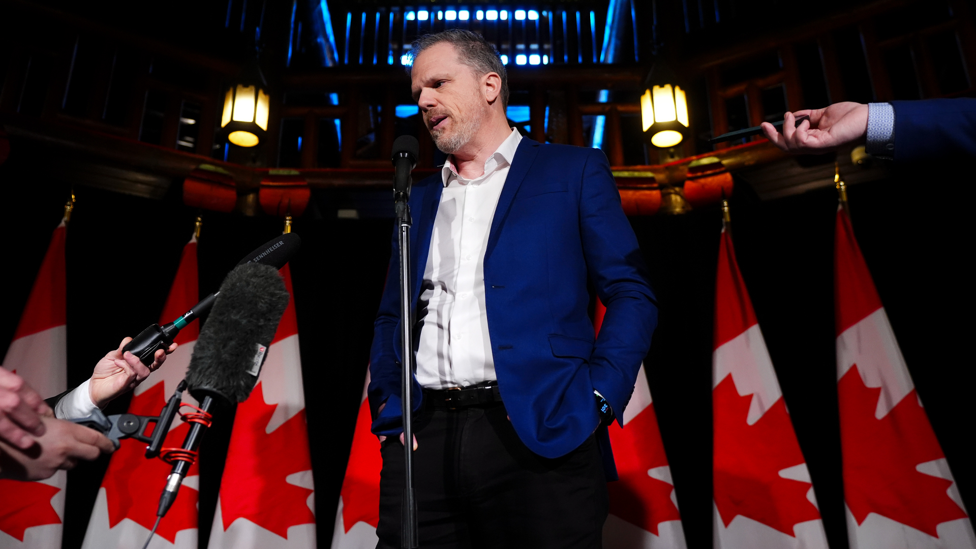 Mark Holland stands in front of Canadian flags and answers questions from journalists who hand him their microphone