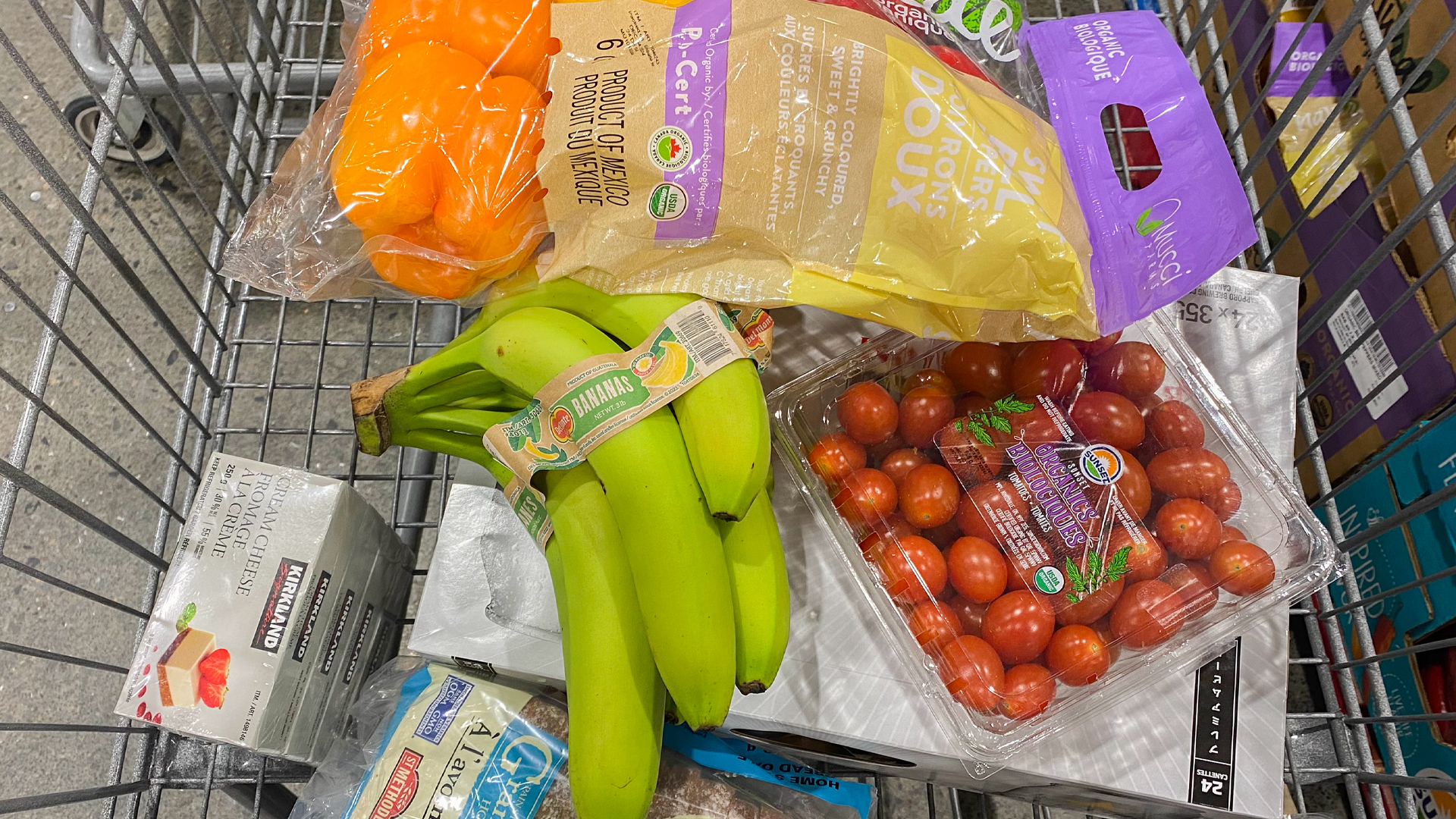 Bananes, tomates cerises, poivrons orange et autres produits d'épicerie dans un panier.