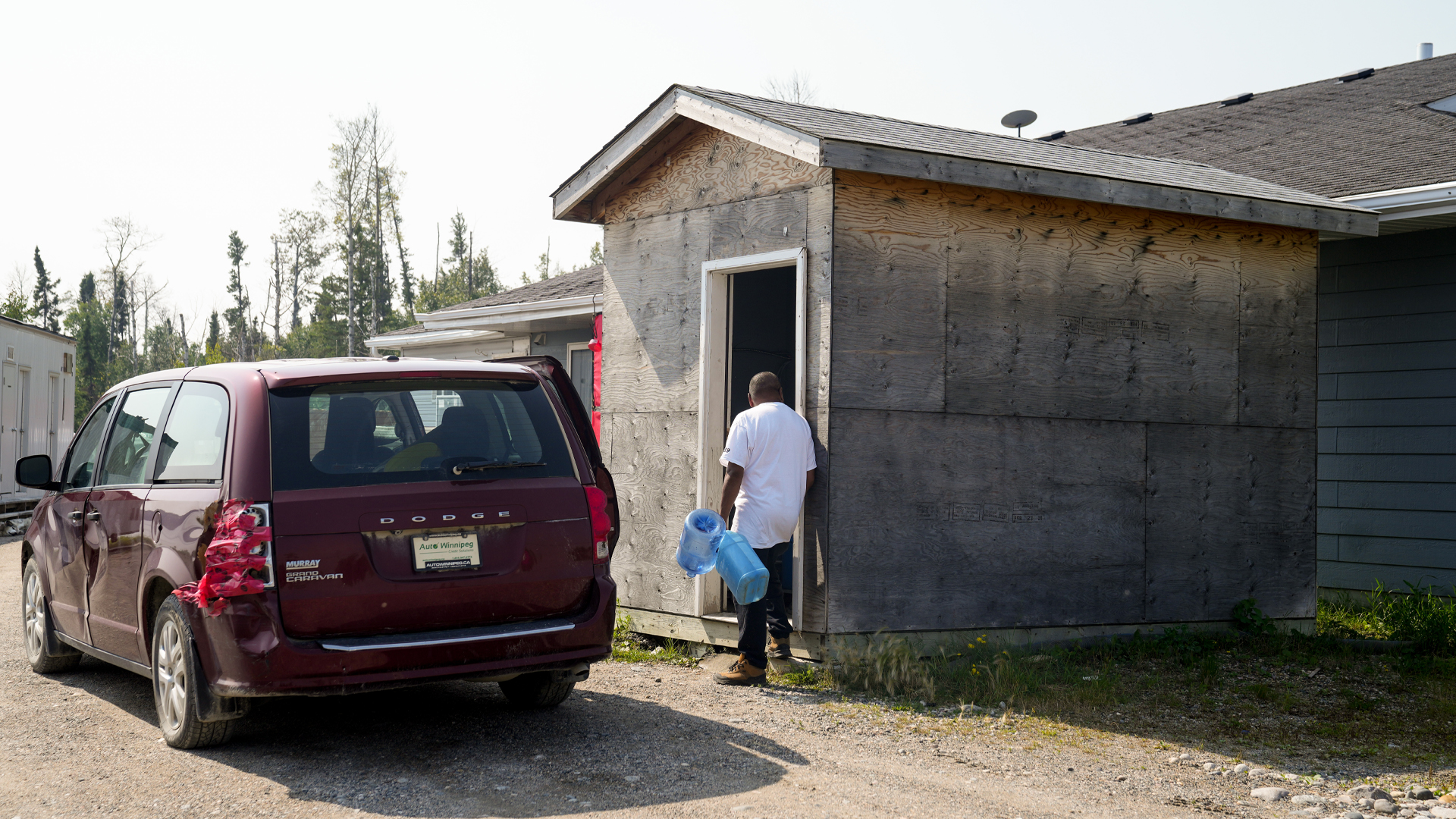 A man carries jugs into a shed.