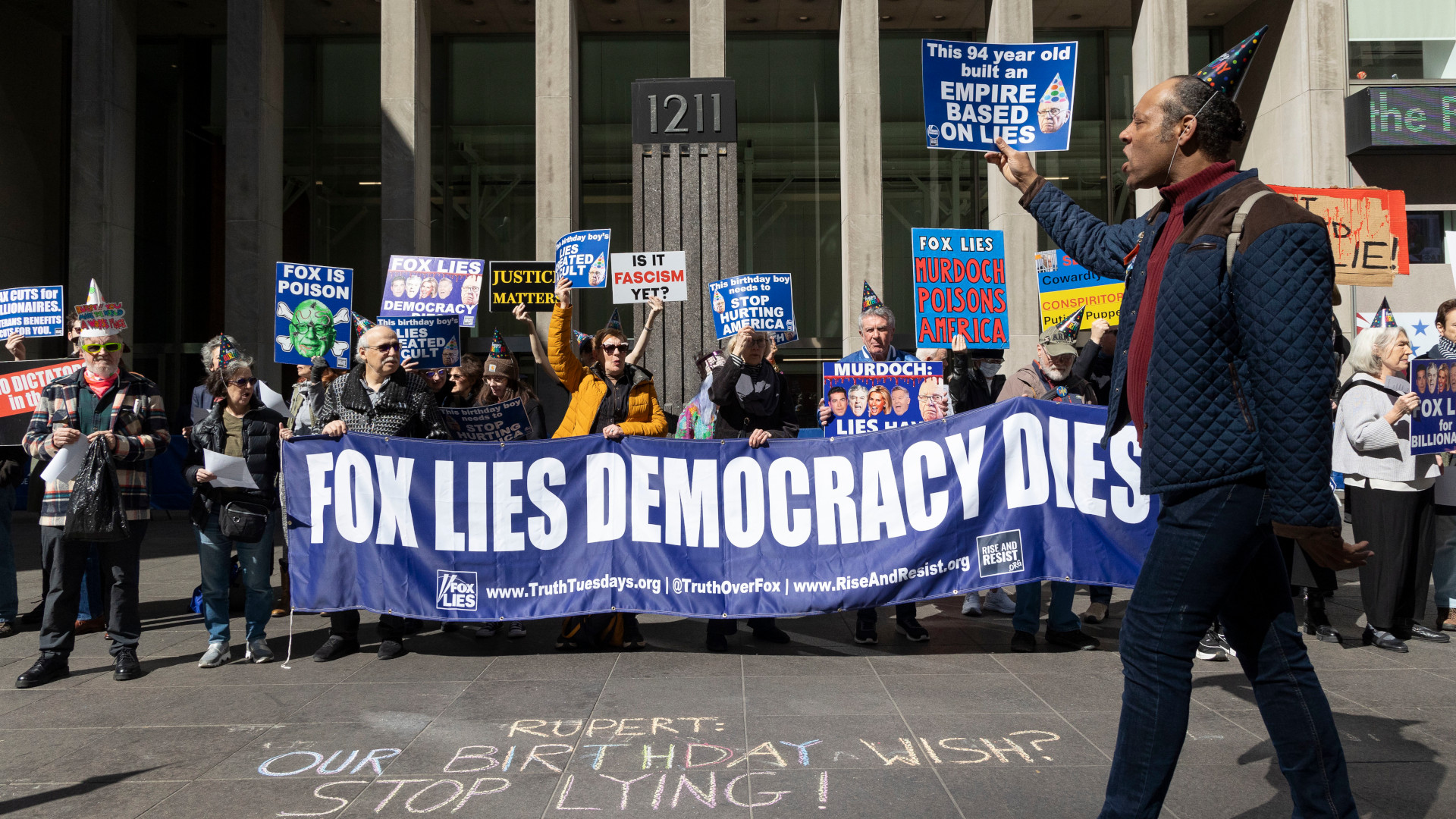 Des manifestants debout devant les bureaux de Fox News tiennent une banderole bleue sur laquelle est écrit en blanc «Fox Lies, Democracy Dies».