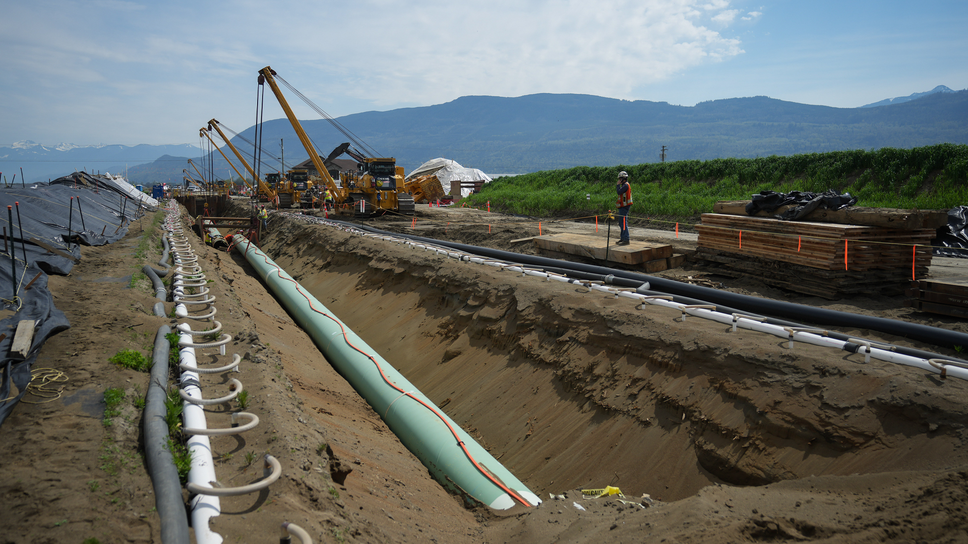 Cranes position green-coloured pipes with mountains in the background.