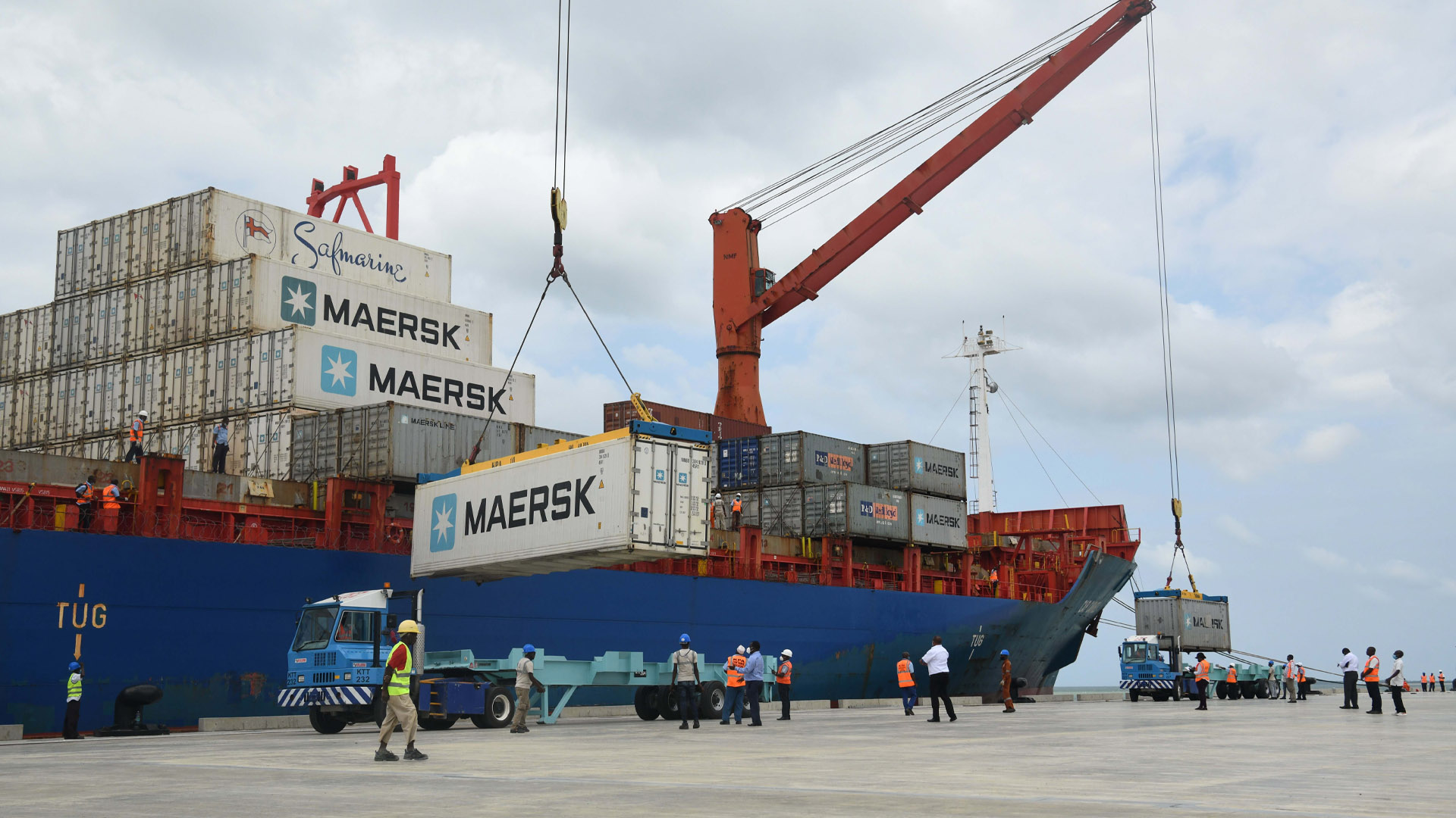 Deux grues déchargent des conteneurs blancs marqués Maersk d'un cargo bleu sur un nouveau quai en béton bien rangé.