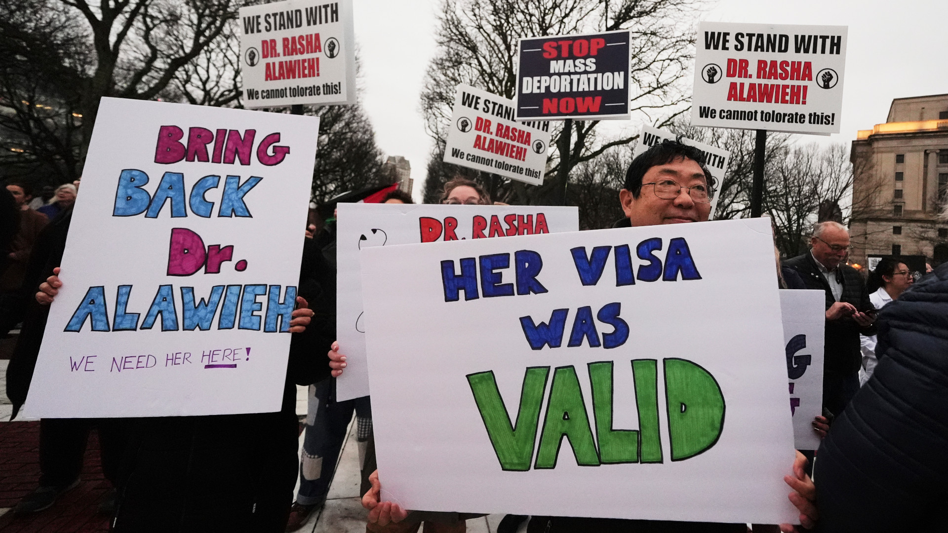 Protesters hold up signs demanding the release of Dr. Rasha Alawieh with messages like “her visa was valid.”