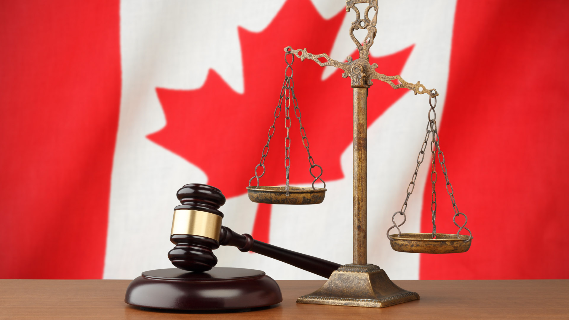 Golden scales of justice and a judge’s gavel in front of a Canadian flag.