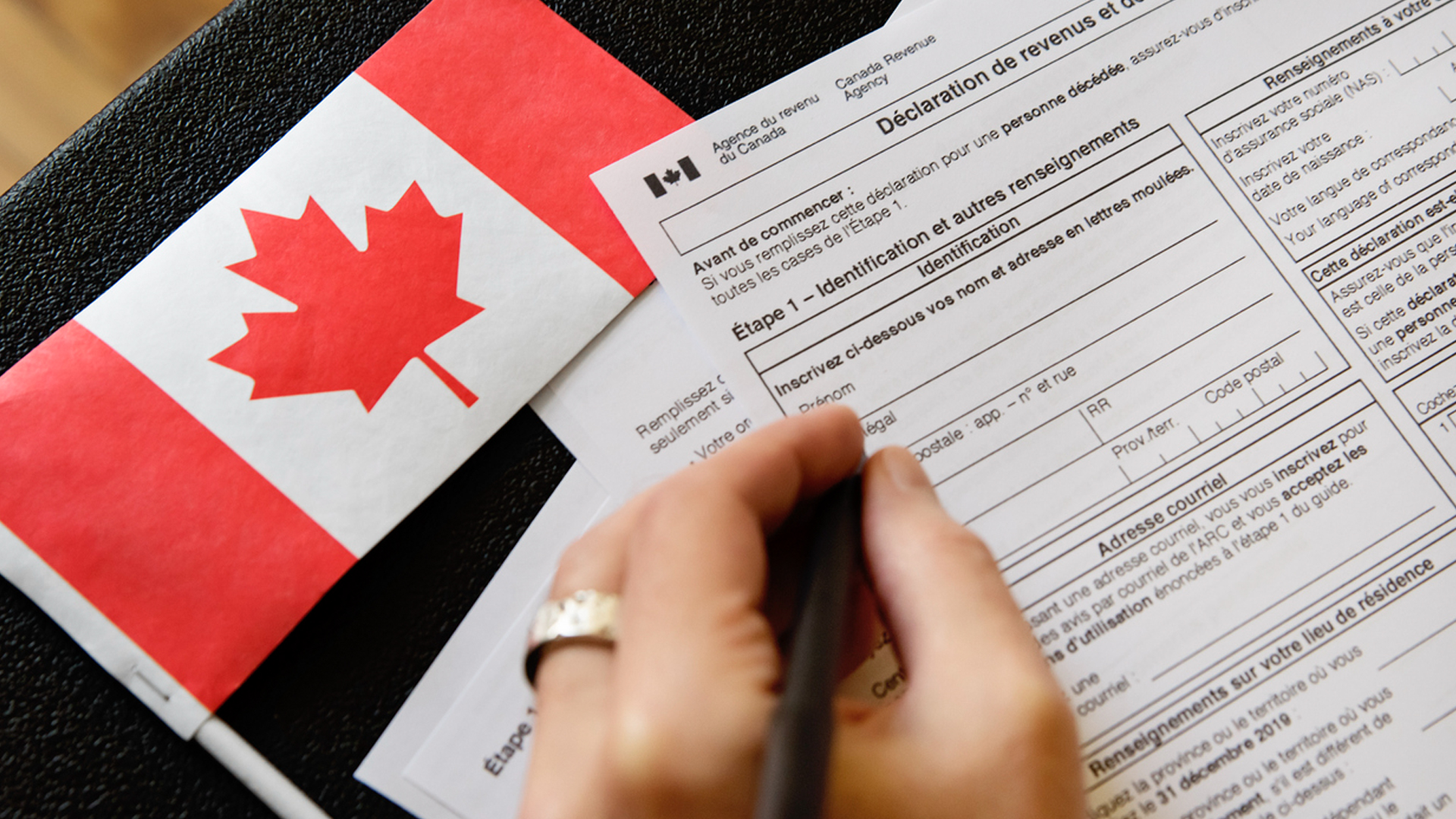 A man fills out Canadian tax documents by hand with a Canadian flag on table.