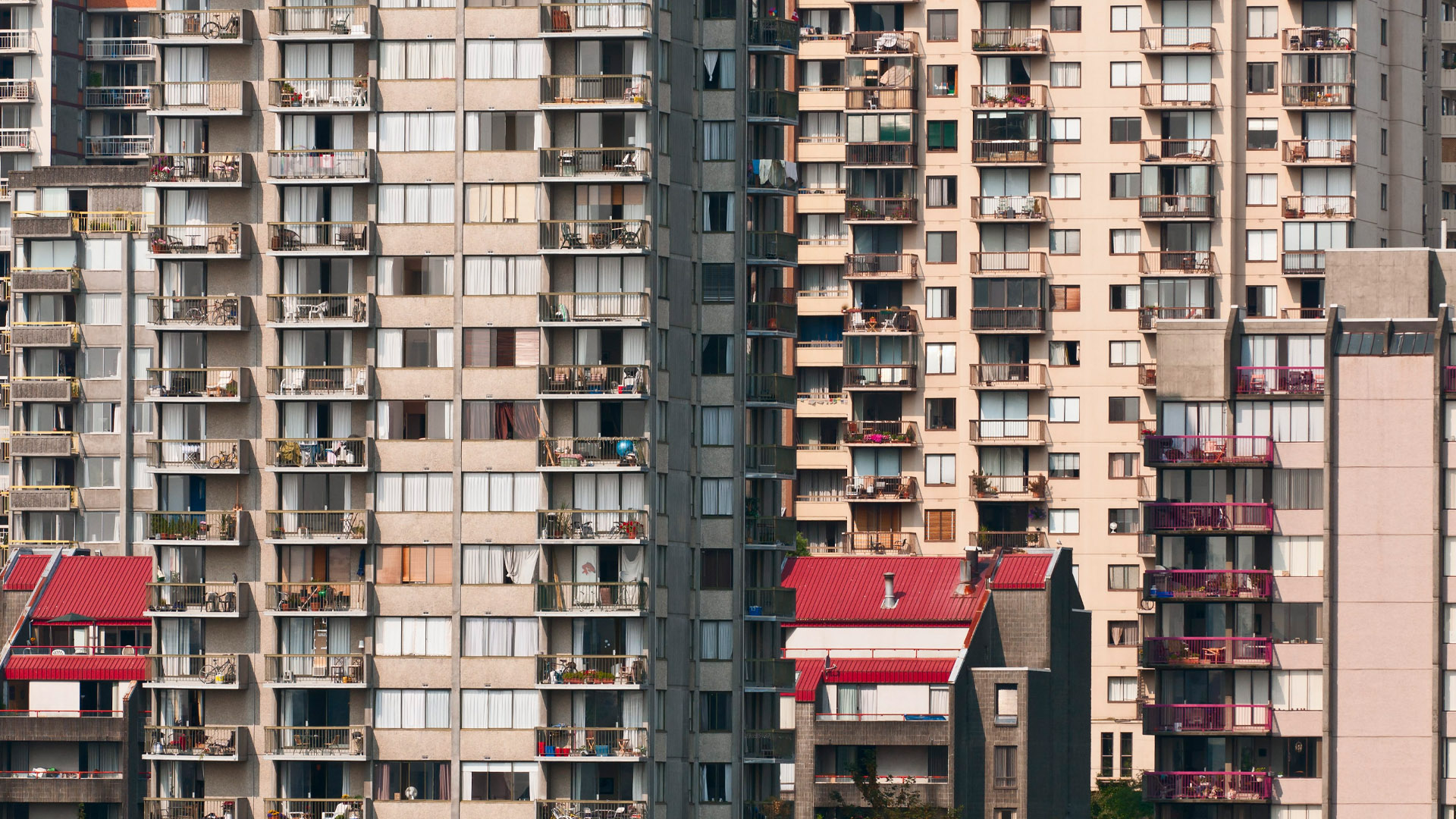 Four high-rise buildings are clustered together with small balconies filled with flower pots, chairs, etc.